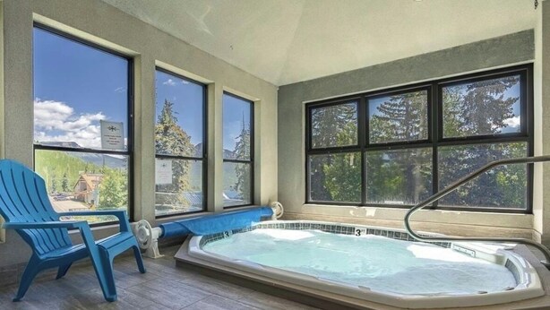 A hot tub in a room with large windows, a blue chair, and a view of trees and mountains. - Recently Renovated Ski In-Out on Purgatory Mountain (Durango)