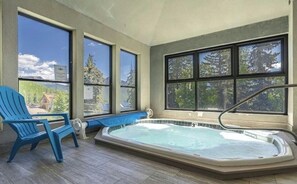A hot tub in a room with large windows, a blue chair, and a view of trees and mountains. - Recently Renovated Ski In-Out on Purgatory Mountain (Durango)