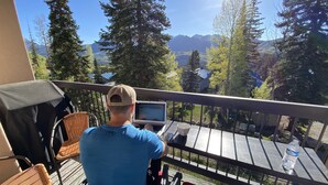 A person seated on a balcony with a laptop, overlooking a mountainous landscape with trees and a clear sky. - Recently Renovated Ski In-Out on Purgatory Mountain (Durango)