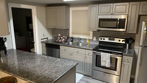 Cozinha moderna com bancadas de granito, eletrodomésticos de aço inoxidável e uma ilha central com banquetas.