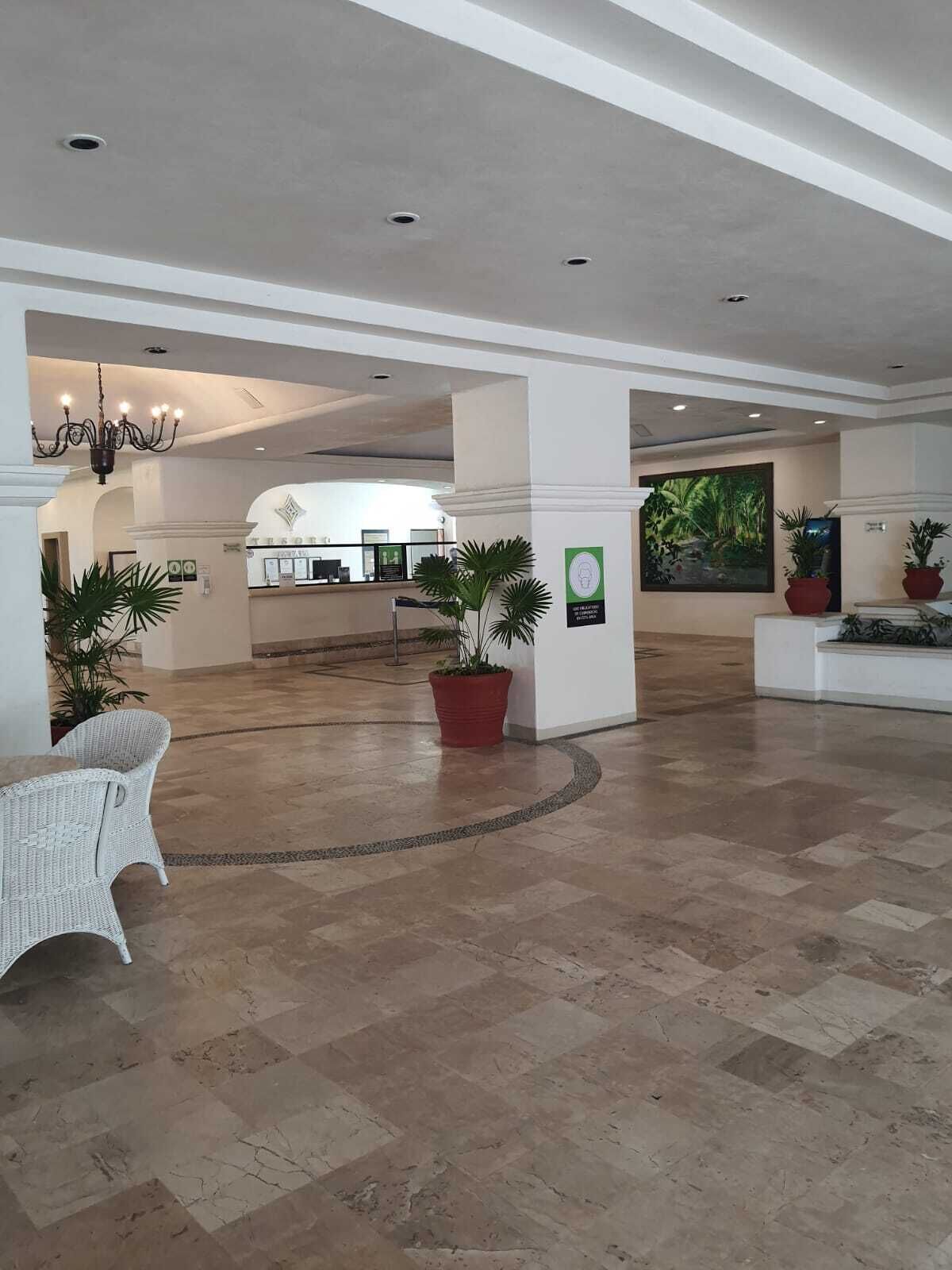 Un lobby espacioso con techo alto, una araña, plantas en macetas y un mostrador de recepción al fondo.