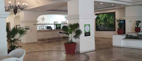Un lobby espacioso con techo alto, una araña, plantas en macetas y un mostrador de recepción al fondo.