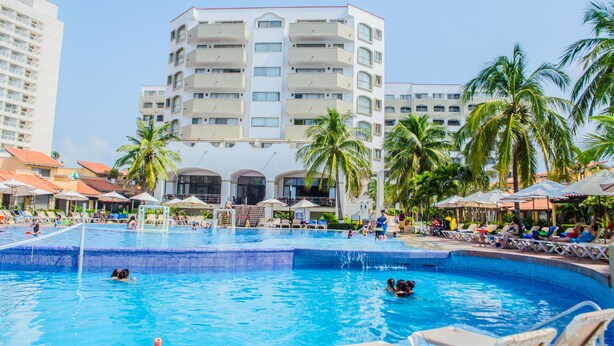 A hotel pool area with multiple levels of balconies, palm trees, and lounge chairs. - Habitación Estándar vista Mar Enna Inn (Ixtapa)