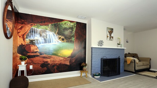 Un salon avec une grande fresque représentant une cascade, une cheminée, un canapé et une table basse.