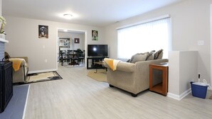Un salon avec un canapé, un téléviseur et, au fond, un coin repas.