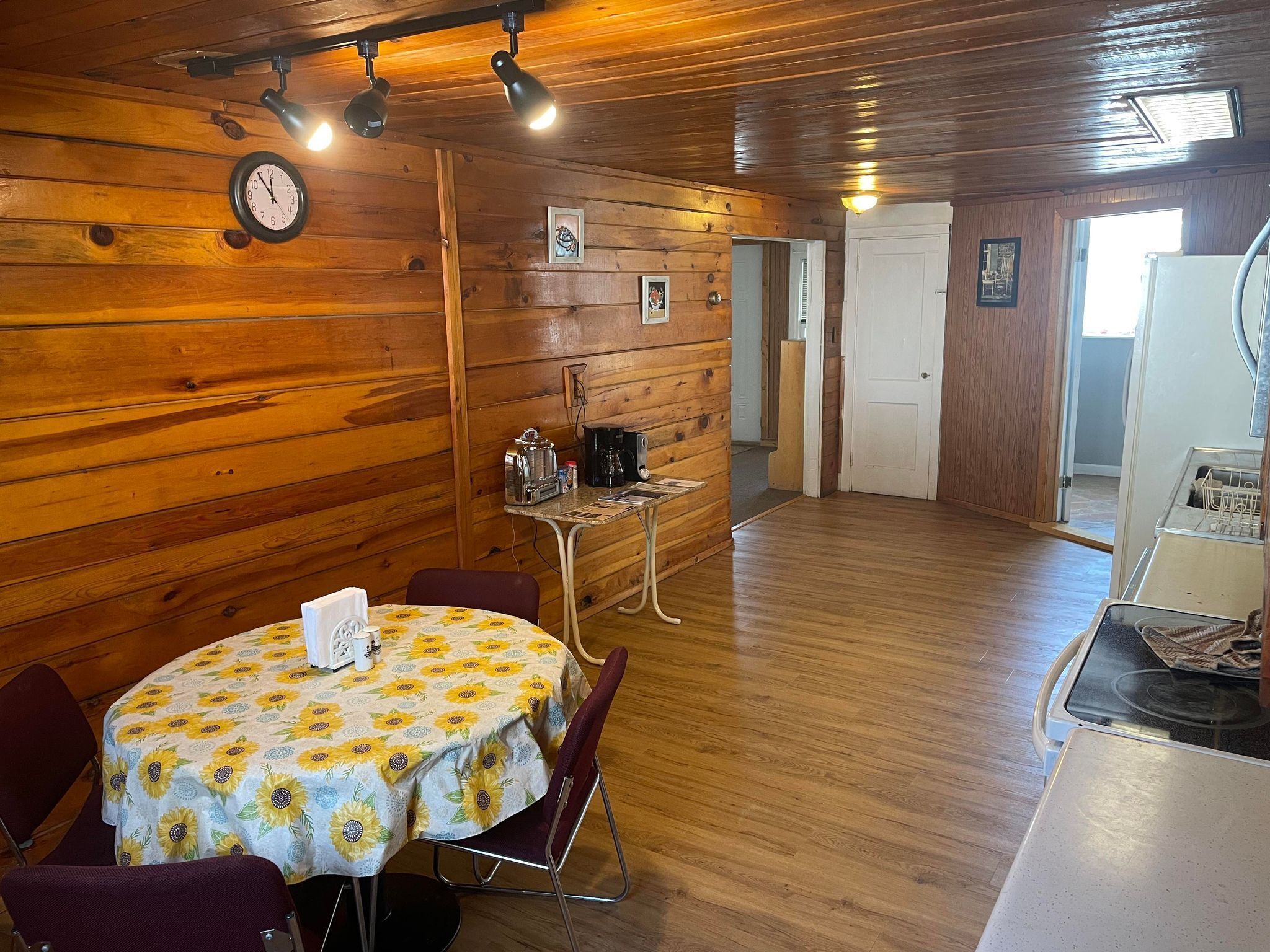 A cozy room with wooden walls, a round table with a floral tablecloth, and a clock on the wall.