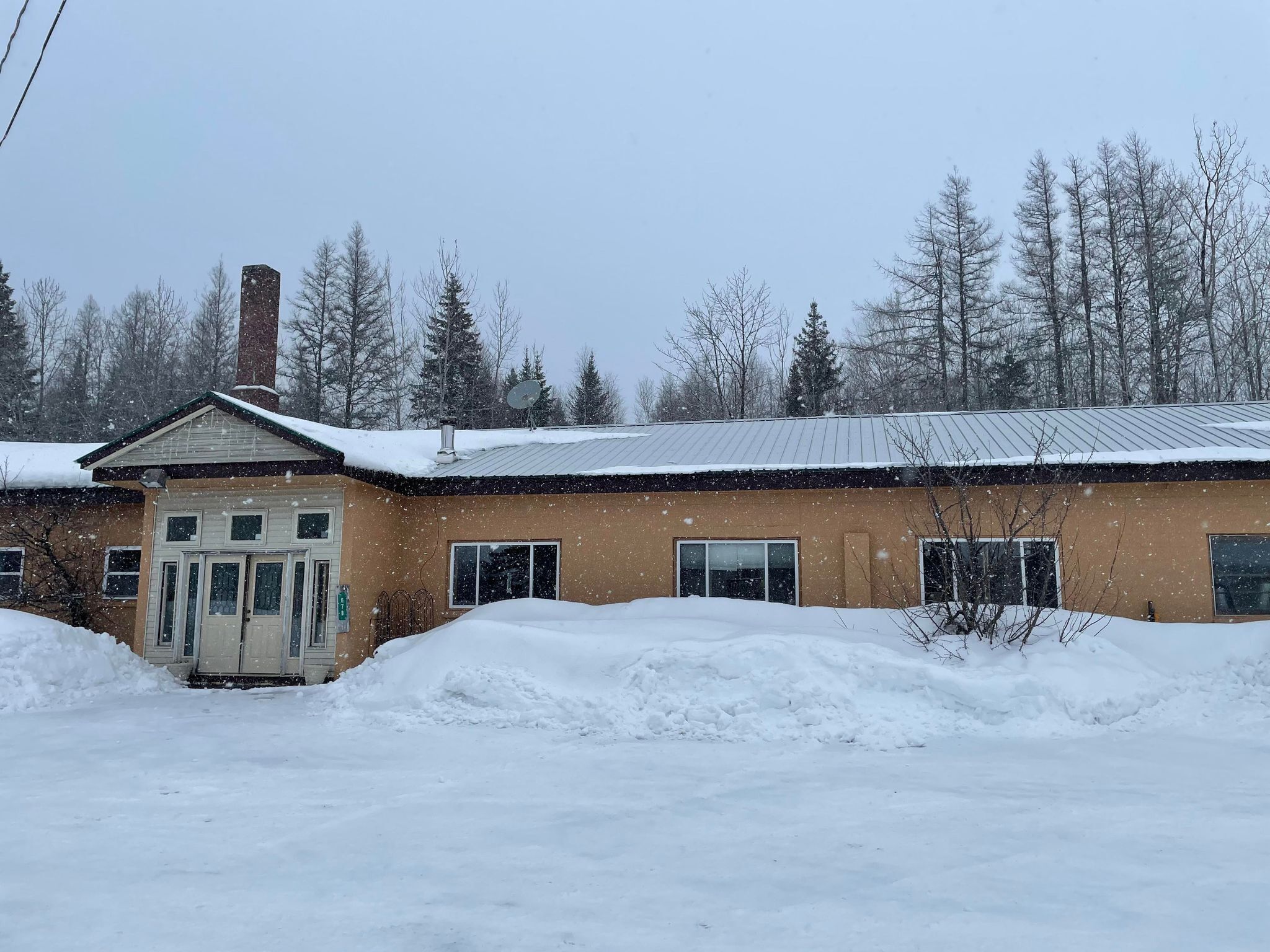 En bygning med brun facade, et metal tag og en skorsten. Der er sne på taget og omkring bygningen.
