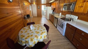 L’intérieur d’un chalet en bois comprend une table à manger, des chaises, une cuisine équipée d’une cuisinière, d’un four et d’un four à micro-ondes, ainsi qu’une horloge au mur.