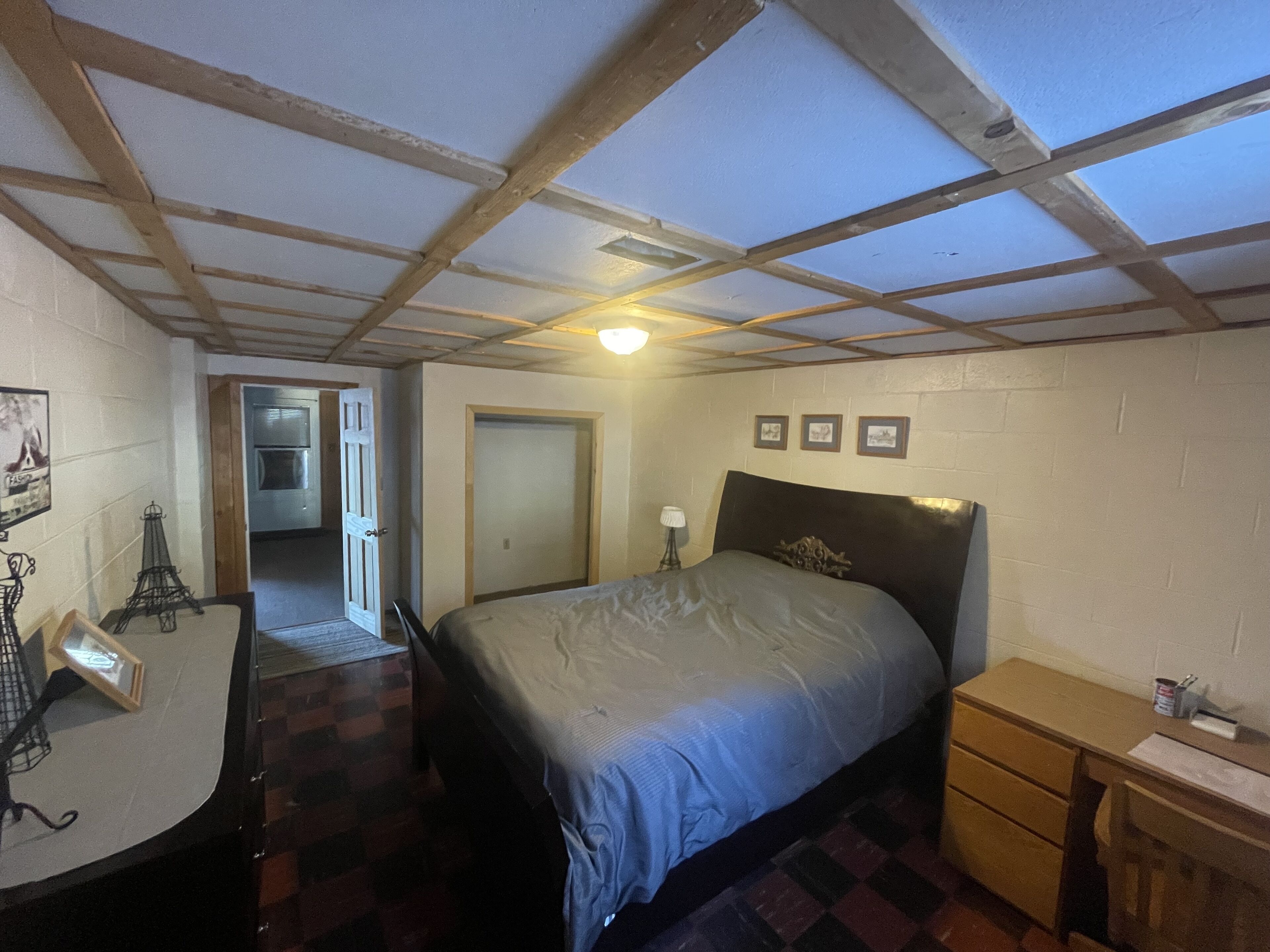 Un dormitorio con cama, escritorio, silla, cómoda y puerta que da a otra habitación.