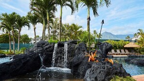 Un resort tropical con una cascada natural de roca, palmeras y una zona de piscina.