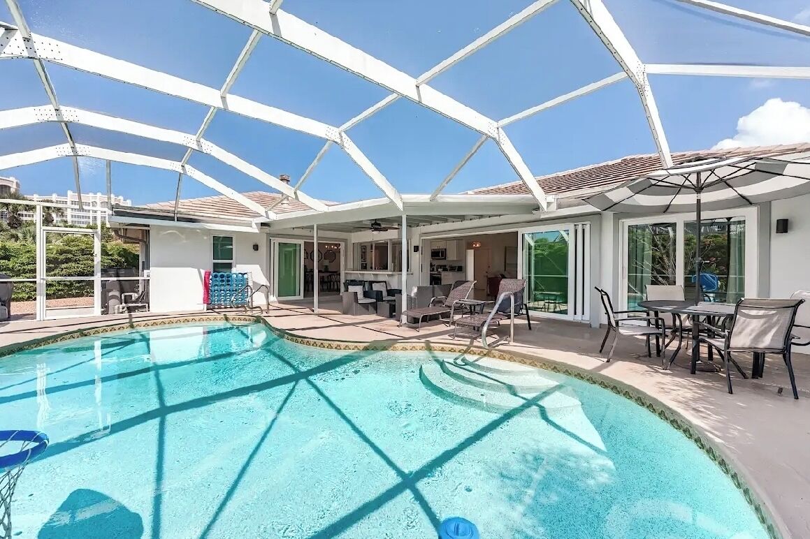 Un área de piscina con techo de cristal, sillones reclinables y zona de comedor.