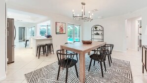 A spacious dining area with a wooden table and black chairs, a chandelier, and a patterned rug.
