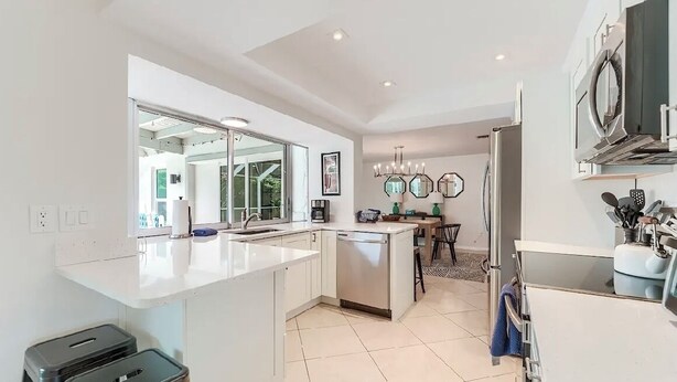 A modern kitchen with white cabinetry, a central island, and a dining area with a chandelier.