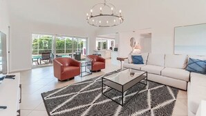 A spacious living room with a modern chandelier, a white sofa, a glass coffee table, and a patterned rug.