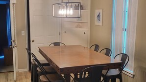 Un coin repas avec une table et des chaises en bois, un luminaire suspendu et une fenêtre avec des stores.