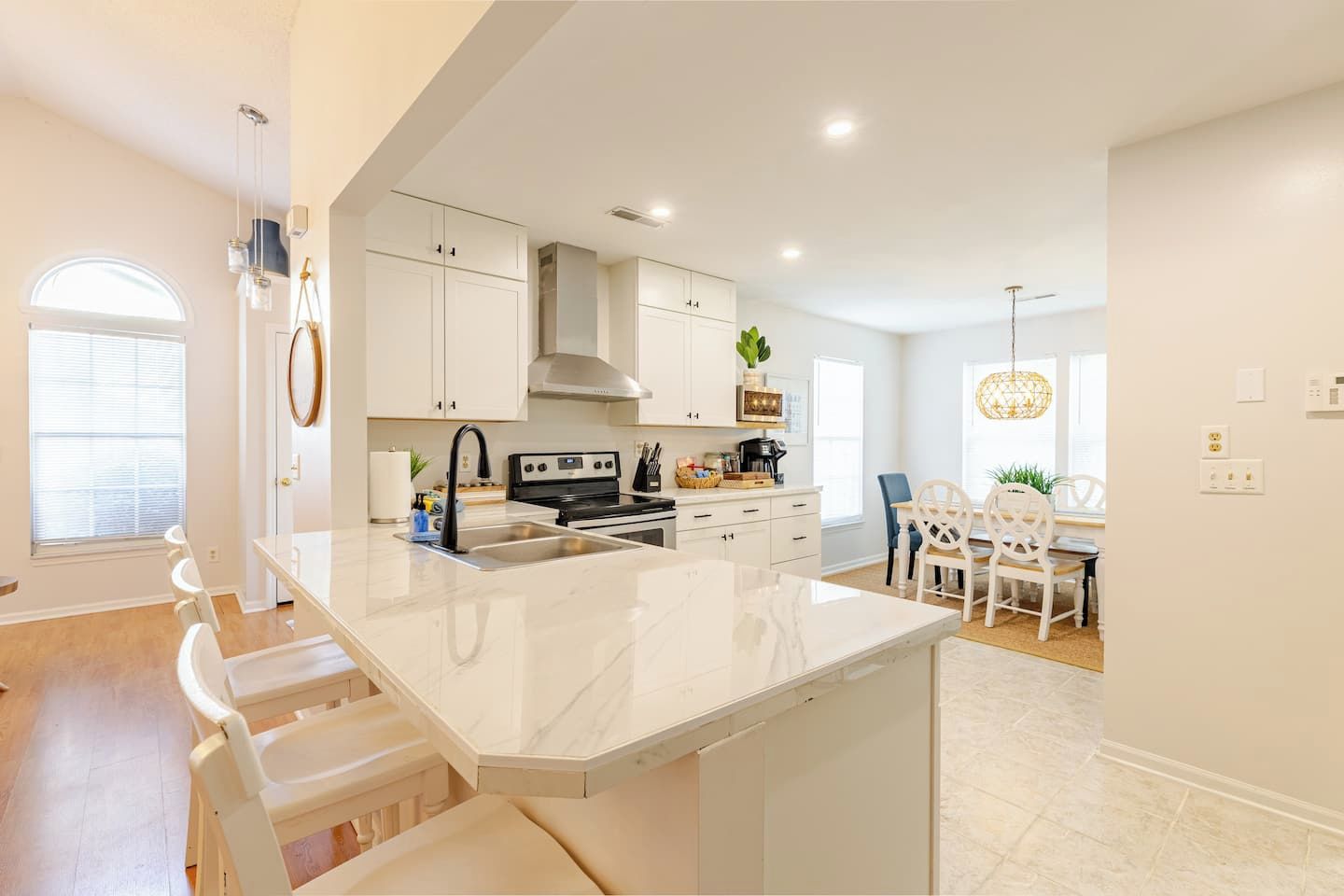 Una cocina moderna con armarios blancos, una isla central y un comedor con sillas blancas.
