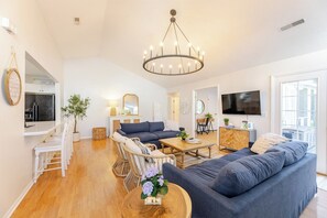 Een ruime woonkamer met een grote bank, een eethoek met witte stoelen, een houten salontafel en een kroonluchter.