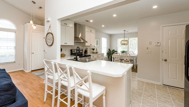 A modern kitchen with white cabinetry, a central island with bar stools, and a dining area with a white table and chairs. - Clean Coastal Cottage 5min to beach & 20 min to Charleston (Mount Pleasant)