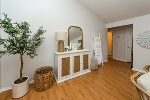 A room with a wooden floor, a white cabinet with a mirror, a potted plant, and a wicker basket.