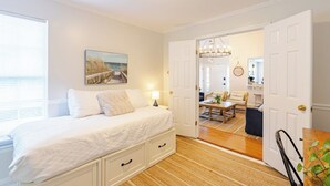 A bedroom with a bed, bedside table, and a view into the living area.