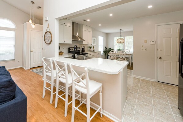 A modern kitchen with white cabinetry, a central island with bar stools, and a dining area with a white table and chairs.