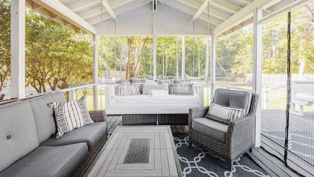 A covered outdoor seating area with a sofa and chairs, a ceiling fan, and a view of trees.
