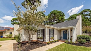 A single-story house with a front porch, a blue door, and solar panels on the roof.