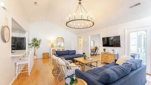 A spacious living room with a large sofa, a dining area with white chairs, a wooden coffee table, and a chandelier. - Clean Coastal Cottage 5min to beach & 20 min to Charleston (Mount Pleasant)