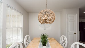 A dining room with a wooden table, white chairs, a hanging wicker chandelier, and a potted plant. - Clean Coastal Cottage 5min to beach & 20 min to Charleston (Mount Pleasant)