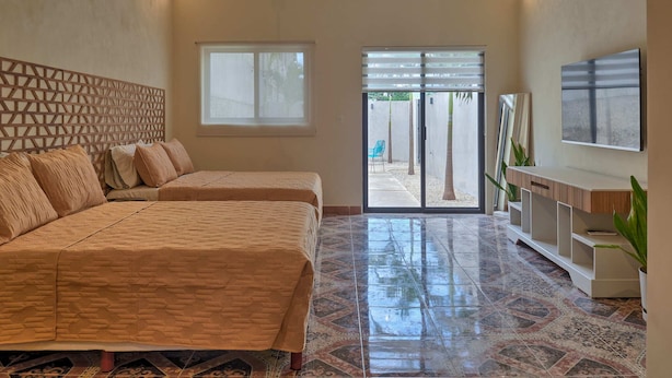 A spacious bedroom with two beds, a large window, a sliding glass door leading to a patio, and a mounted TV. - La Ermita Suites in Merida Centro with Pool - Historic Church Front (Centro)