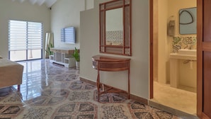 A spacious living area with a large window, a television, a wooden console table, and a bathroom with a sink and mirror. - La Ermita Suites in Merida Centro with Pool - Historic Church Front (Centro)