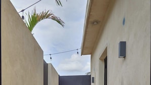A narrow pathway leading to a dark door, flanked by light-colored walls and a string of lights. - La Ermita Suites in Merida Centro with Pool - Historic Church Front (Centro)