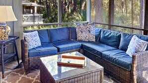 A covered outdoor seating area with a wicker sofa, a glass coffee table, and a lamp. - Pet Friendly, Walk to beach, pool and community dock and more! (Kiawah Island)