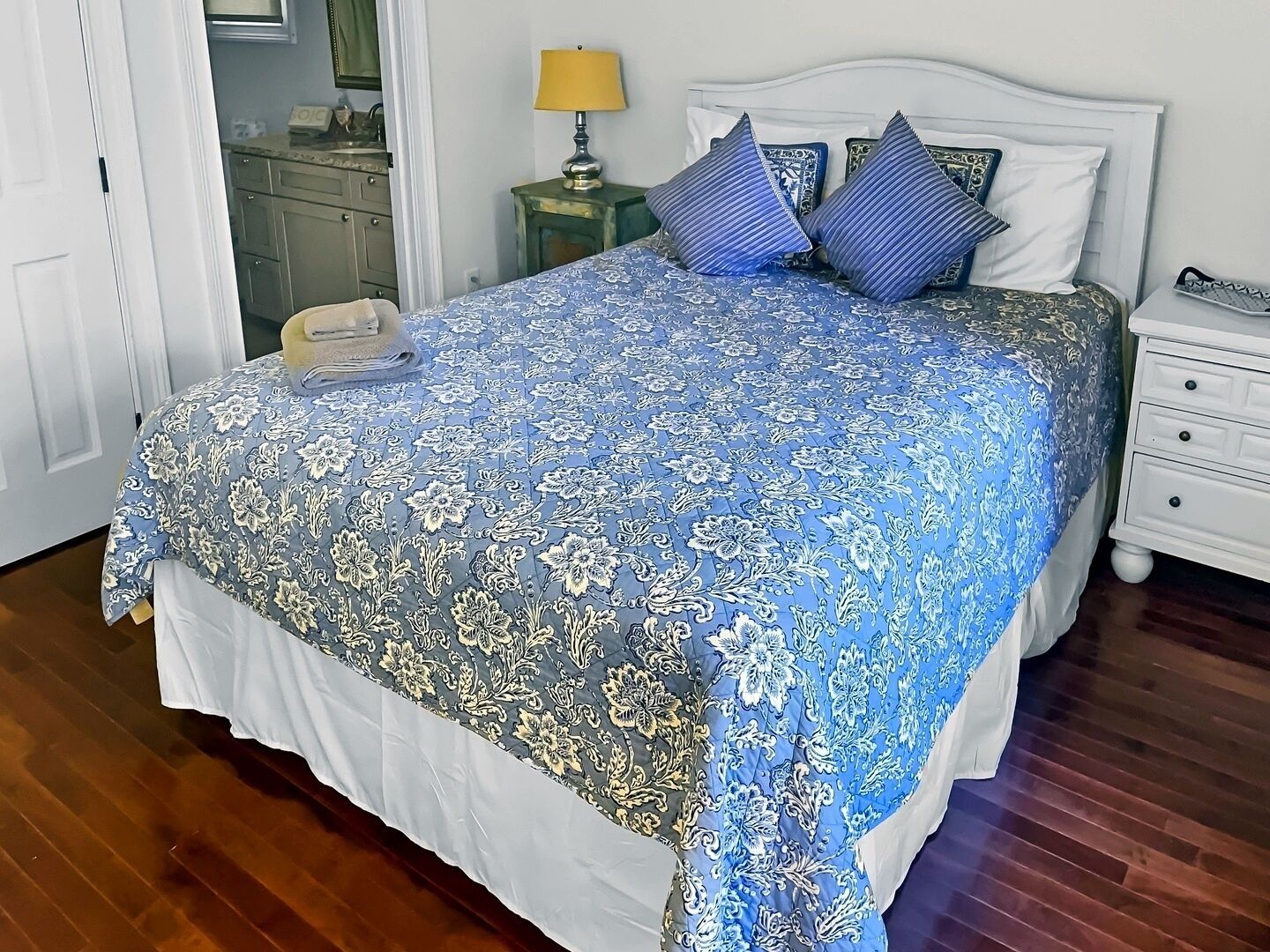 Un lit bien fait, recouvert d’une couvre-lit à motifs floraux, une lampe de chevet et une table de chevet avec un téléphone.