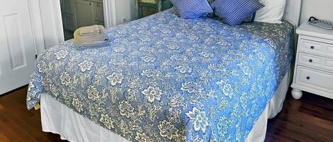 Un lit bien fait, recouvert d’une couvre-lit à motifs floraux, une lampe de chevet et une table de chevet avec un téléphone.