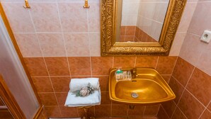 Un baño con un lavamanos dorado, un espejo con un marco ornamentado y una pequeña mesa con una toalla y artículos de aseo.