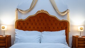 Una cama con cabecera capitonada, dos mesitas de noche con lámparas y cortinas traslúcidas.