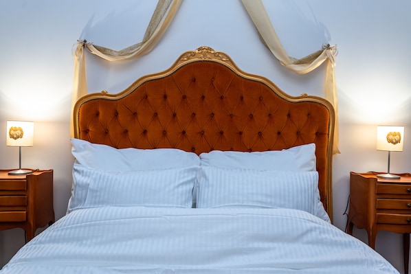 Un lit avec une tête de lit capitonnée, deux tables de chevet avec des lampes et des rideaux légers.