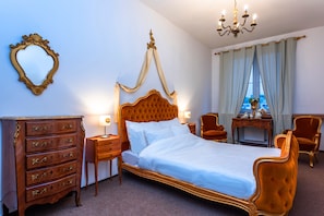 Une chambre à coucher avec un lit à baldaquin, une commode en bois, une coiffeuse avec un miroir et une fenêtre avec des rideaux.