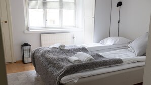 Un dormitorio con dos camas, una ventana con persianas, un radiador, una mesita de noche con una lámpara y una lámpara de pie.