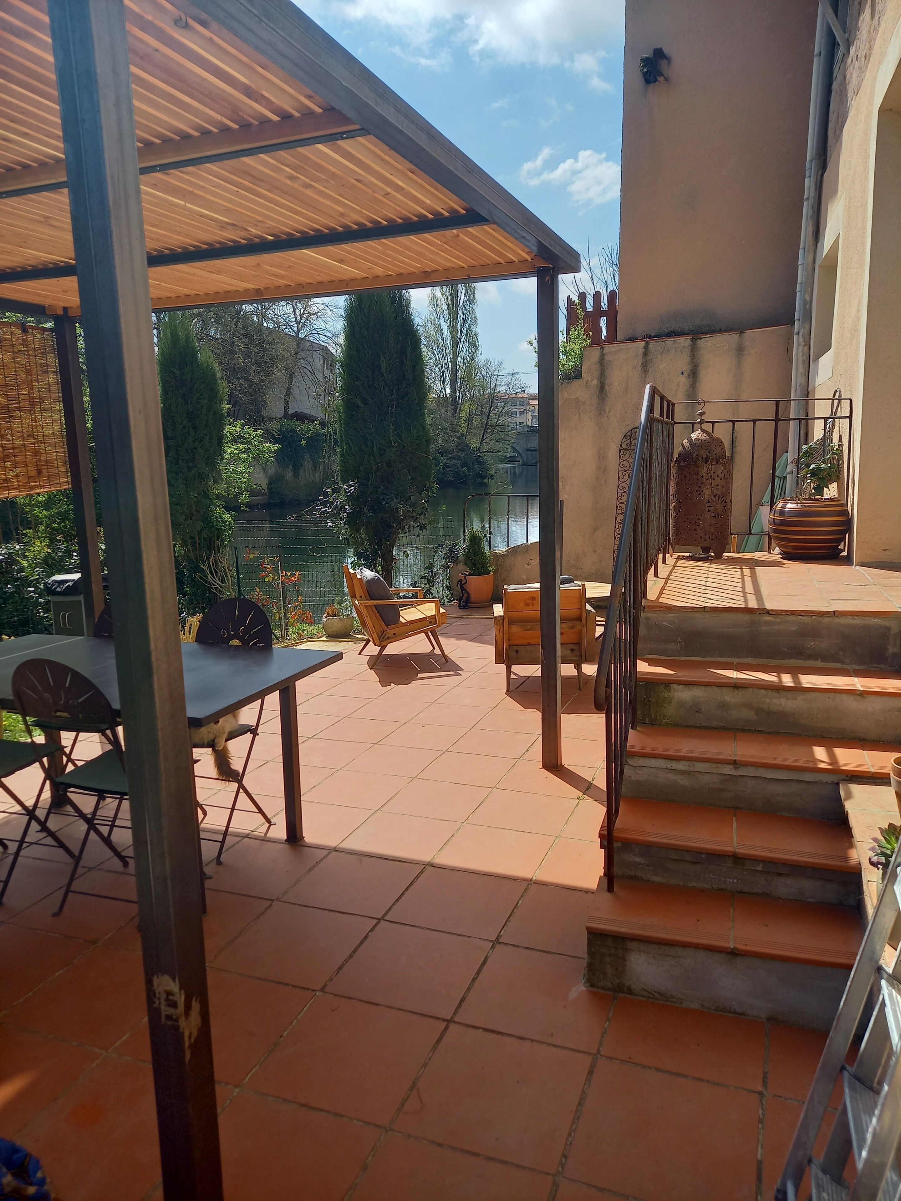 A covered patio area with a table and chairs, a staircase, and a view of a body of water.