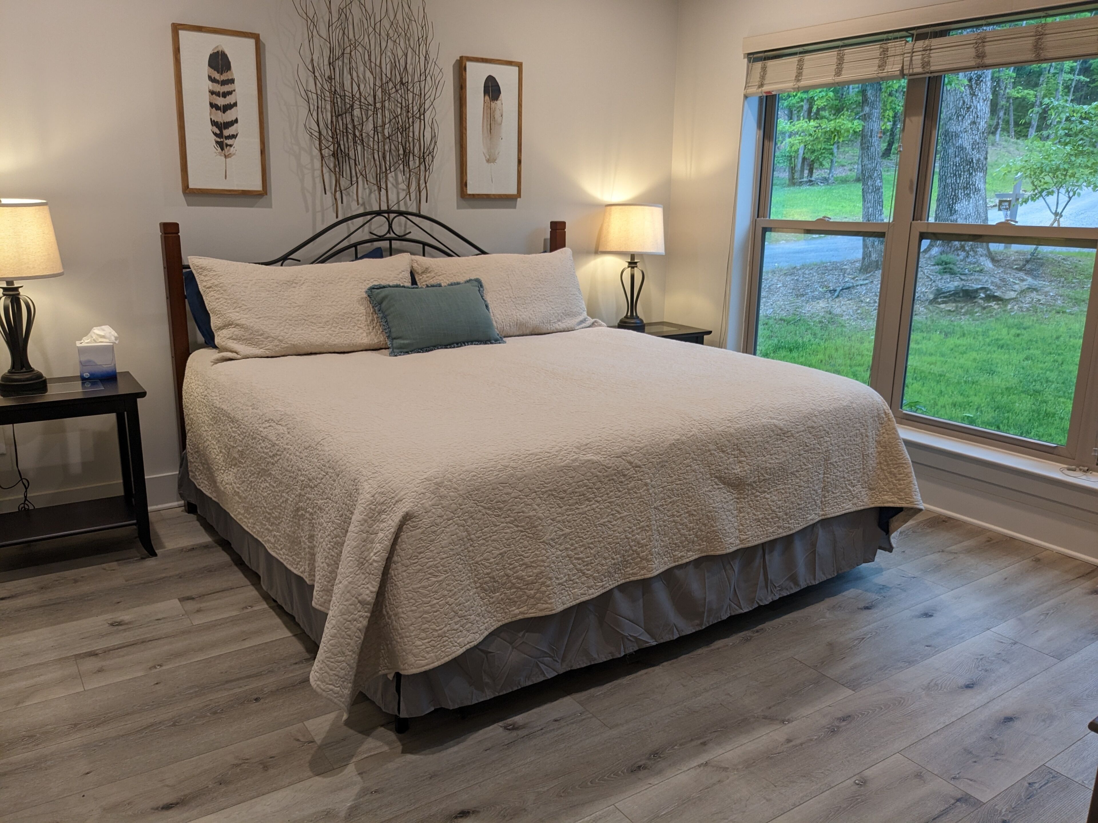 Une chambre à coucher avec un grand lit, deux tables de chevet et une fenêtre donnant sur un paysage verdoyant.