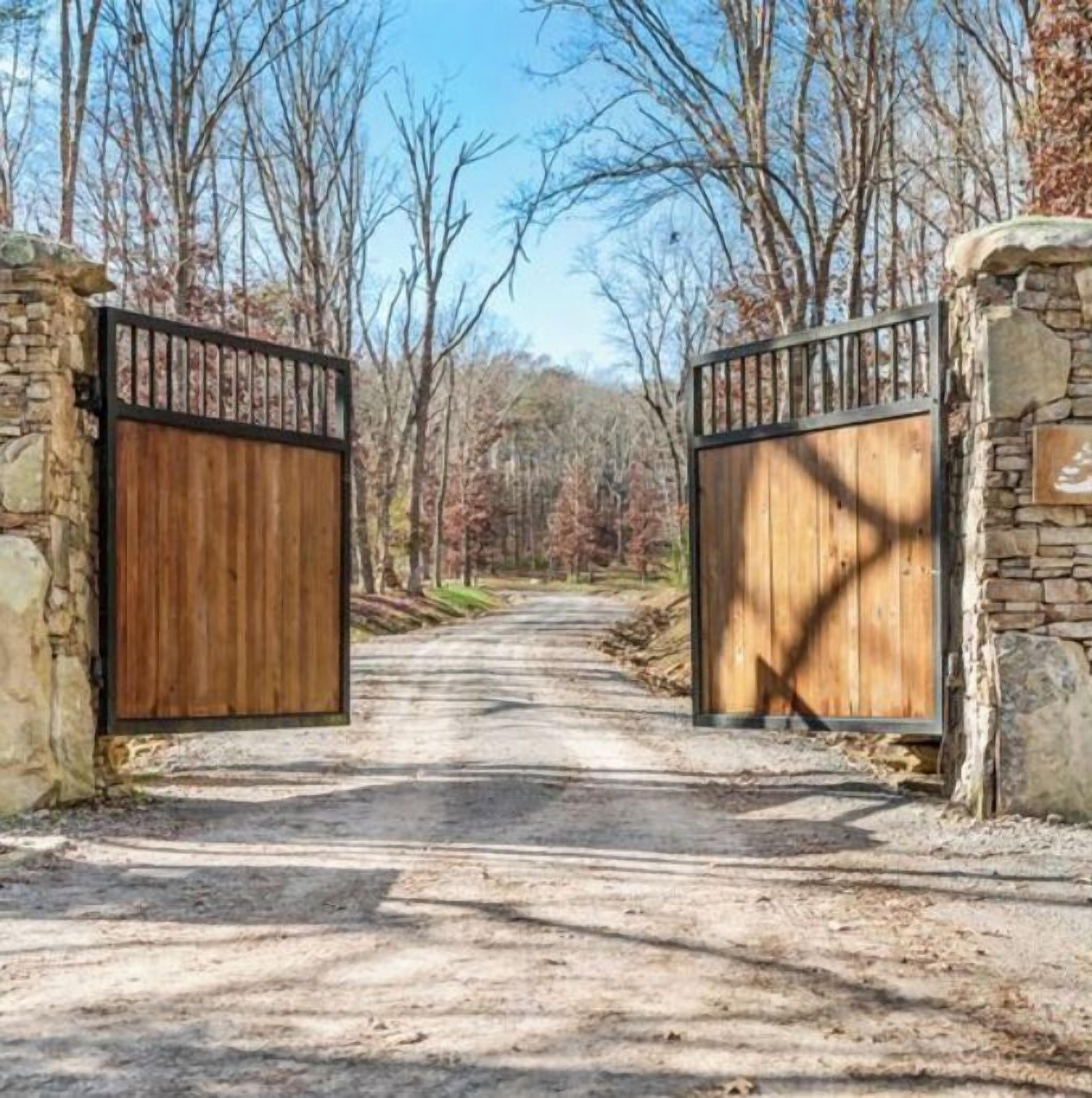 A rustic wooden gate with stone walls, leading into a forested area.