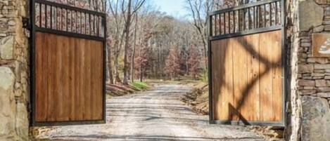 A rustic wooden gate with stone walls, leading into a forested area.