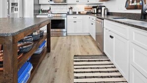 Une cuisine moderne avec des meubles blancs, un îlot central en bois et un tapis à rayures.