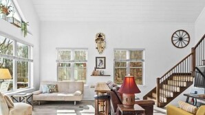 Un vaste salon doté d’un haut plafond, de grandes fenêtres, d’un escalier et d’un assortiment de meubles, notamment un canapé, des fauteuils et une table.