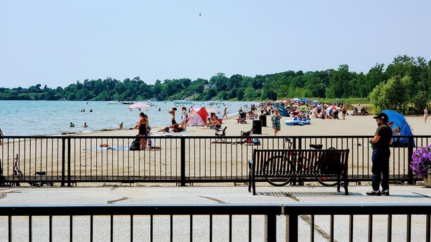 Una playa con gente nadando y tomando el sol, una valla en primer plano y una bicicleta estacionada cerca de la valla.