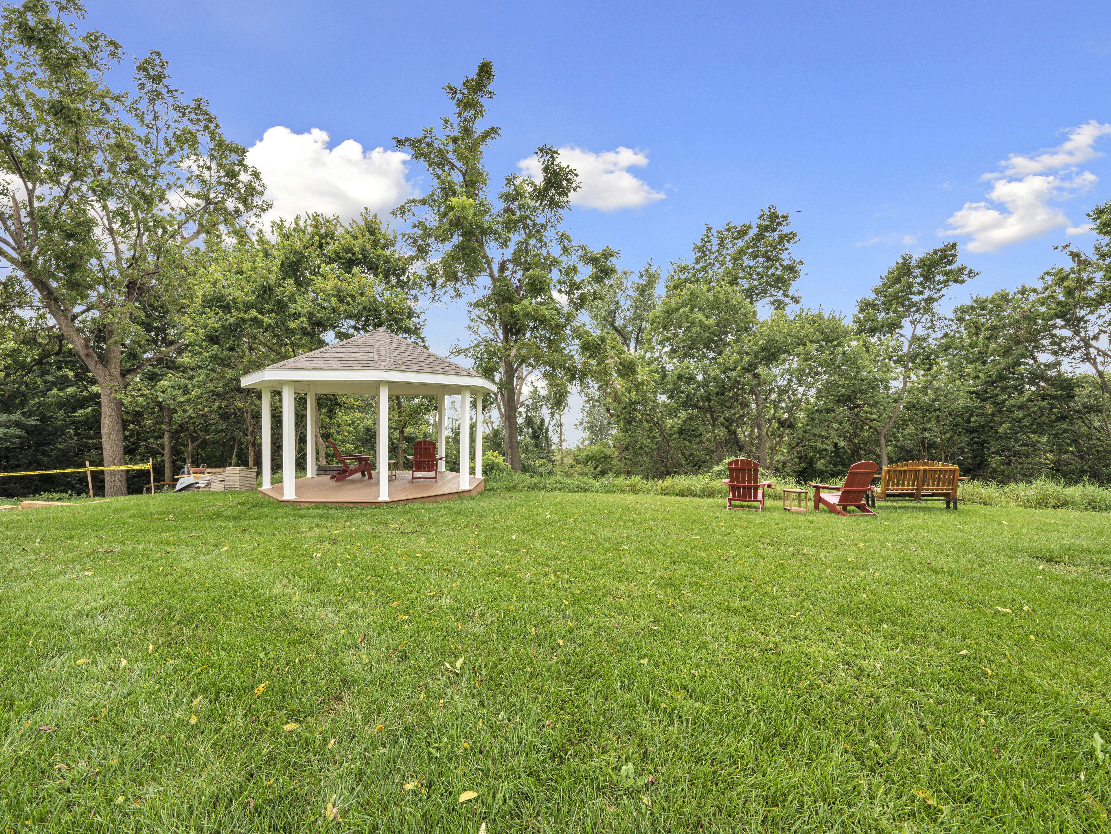 A gazebo with a covered patio, surrounded by a grassy field and trees.