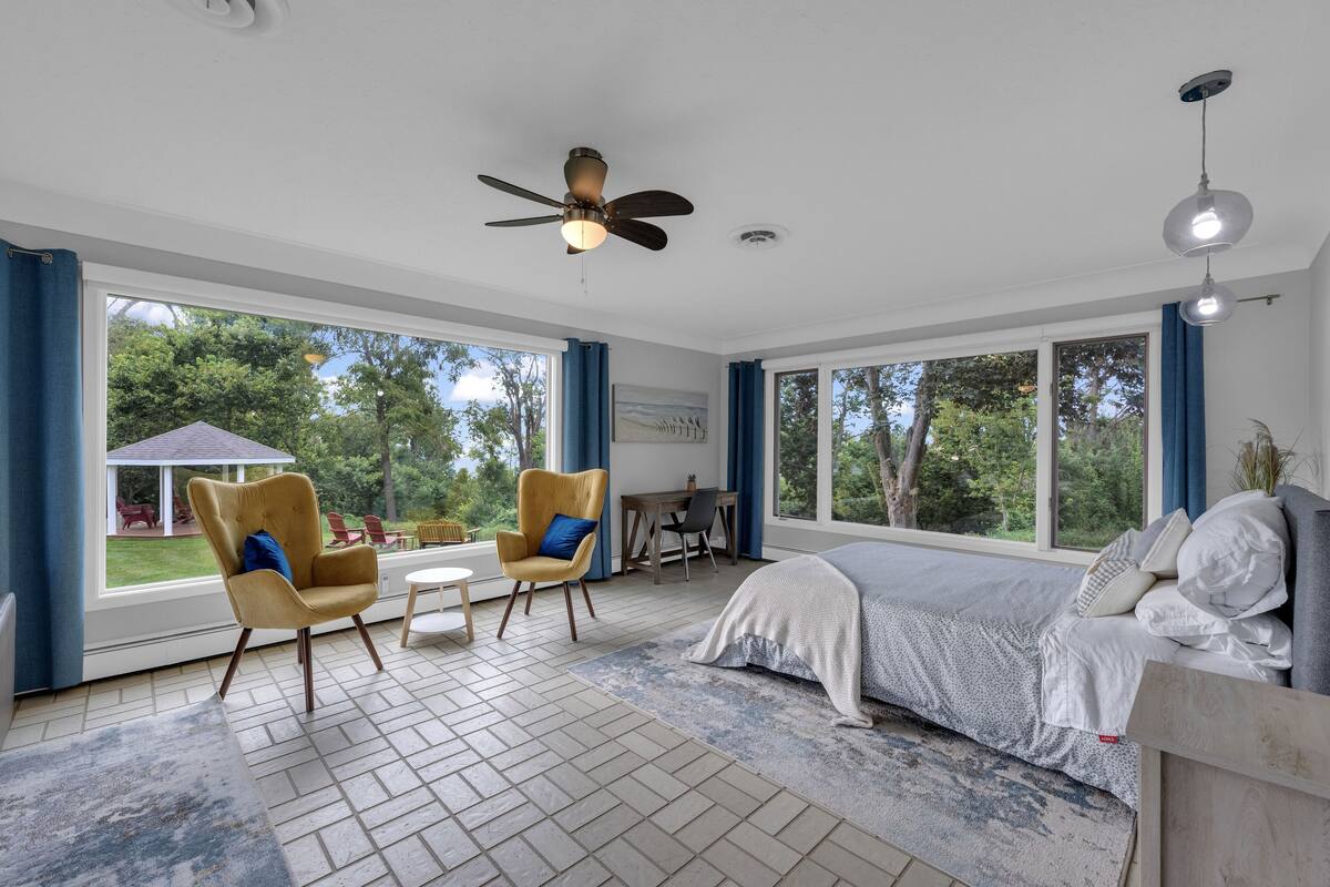 A spacious bedroom with a large bed, two armchairs, a desk, and a ceiling fan.
