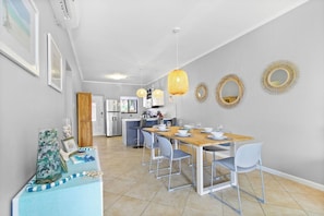 Zona pranzo moderna con tavolo e sedie in legno, una cucina sullo sfondo e specchi decorativi a parete.